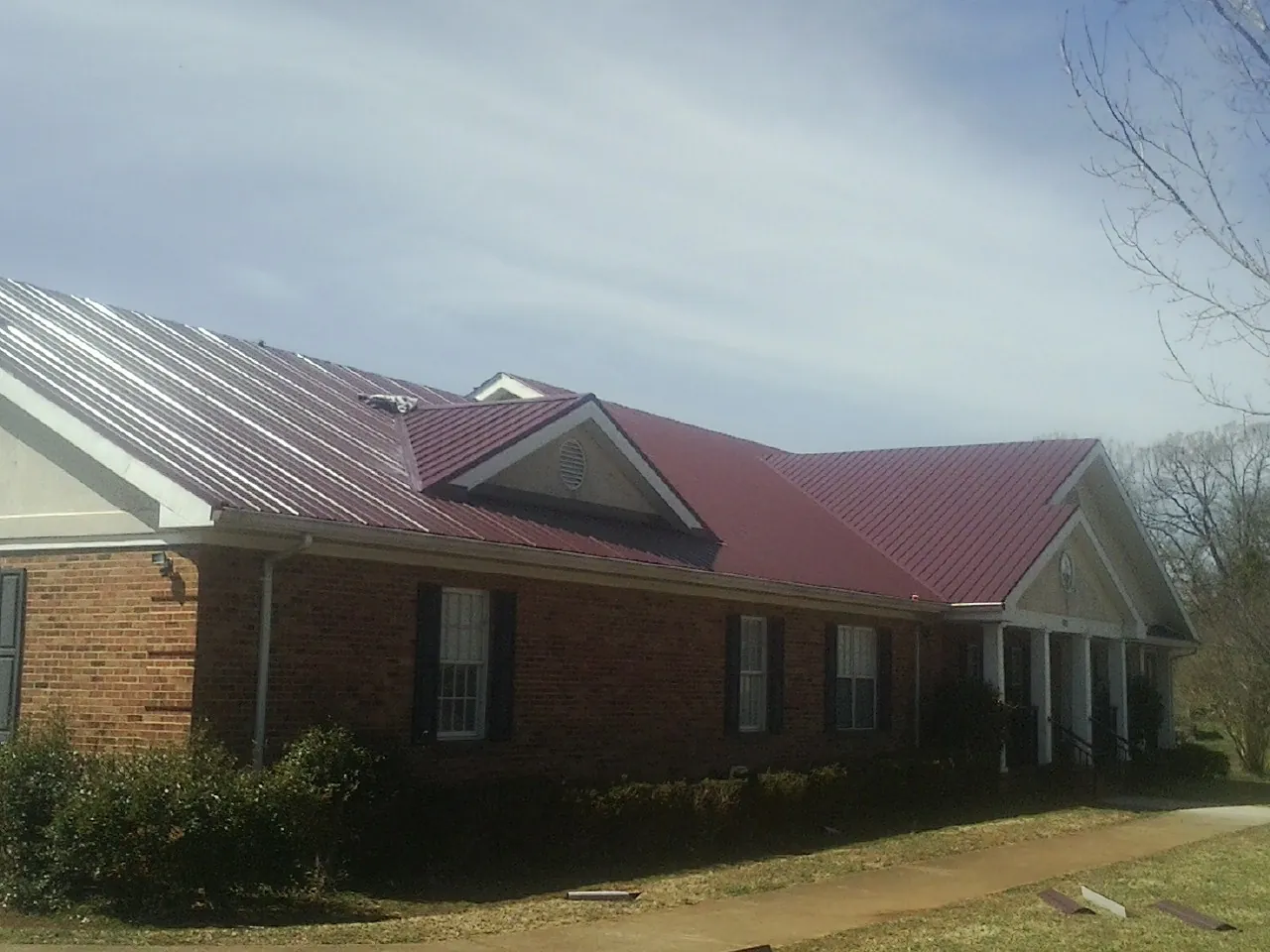 Red metal roof with gabled entries on a long brick building, from a Hail Damage Roof Repair job in Victory Mills