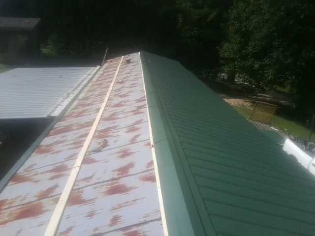 Old rusted panels beside newly installed green metal roofing — Wind Damage Roof Repair by Roofing Brothers in Victory Mills