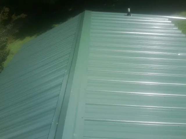 New green metal panels meeting at the ridge of a roof — Flat Roof Repair work by our crew in Victory Mills