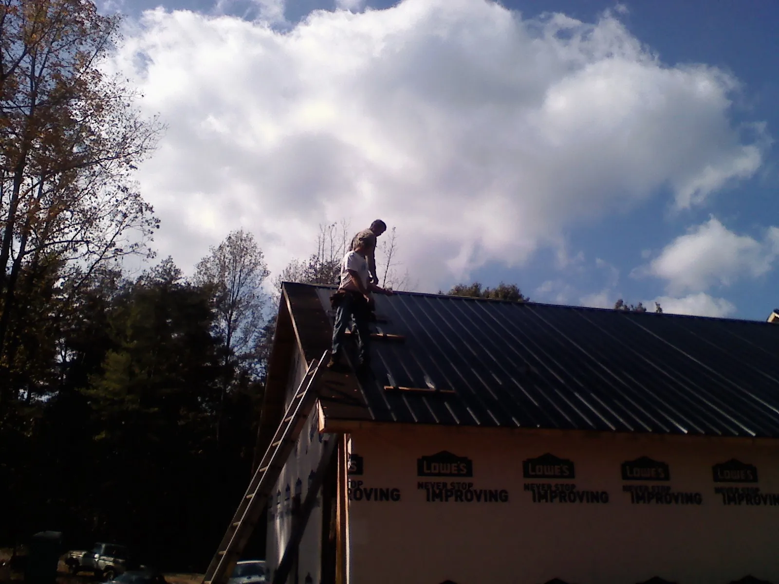 Roofer fastening dark metal panels high against a cloudy sky, from a Roof Inspection job in Victory Mills
