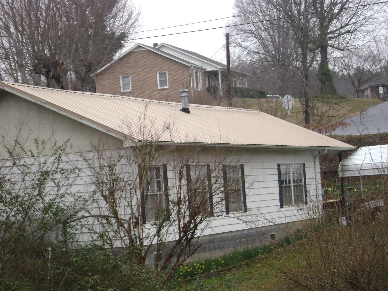 Tan metal roof on a white sided house set into a hillside — Commercial Roofing by Roofing Brothers in Victory Mills